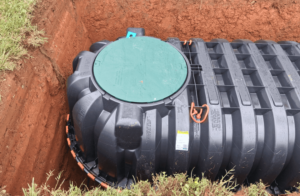 New black plastic septic tank with a green riser lid sitting in a freshly excavated pit