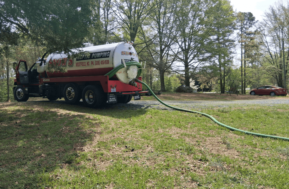 Rear view of the Snow's Septic Pumping tanker truck on a gravel driveway with the vacuum hose connected for a pump-out