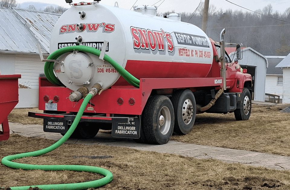 Close-up of the Snow's Septic Pumping truck's white tank with red lettering and the suction hose coiled to the rear